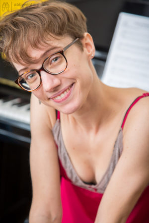 Skinny nerdy girl with short hair displays her unshaved snizz on piano bench